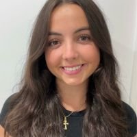Mujer joven con cabello castaño oscuro sonriendo frente a fondo blanco, luciendo una cadena dorada con cruz. rostro humano, profesionalismo, cercanía, juventud, confianza. | Diseño Web – SZ Web Design.