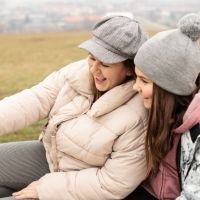 Madre e hija sonrientes tomándose una selfie al aire libre en un día frío, con ropa de abrigo y gorros de lana. - cliente feliz, conexión familiar, experiencia positiva, confianza en el servicio, testimonio visual cálido. | Diseño Web – SZ Web Design.