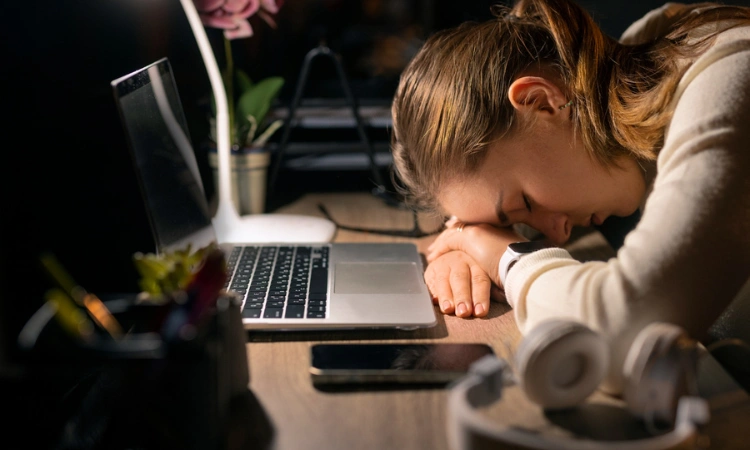 Mujer agotada frente a su computadora portátil tras largas horas de trabajo.