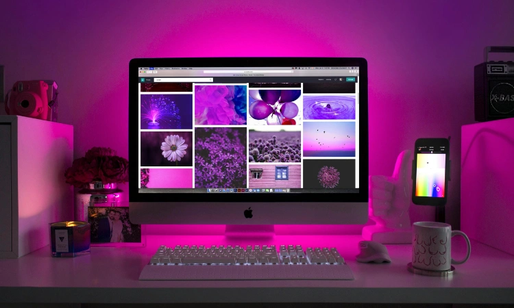 Estación de trabajo con iMac mostrando galería de imágenes creativas en ambiente iluminado en rosa.