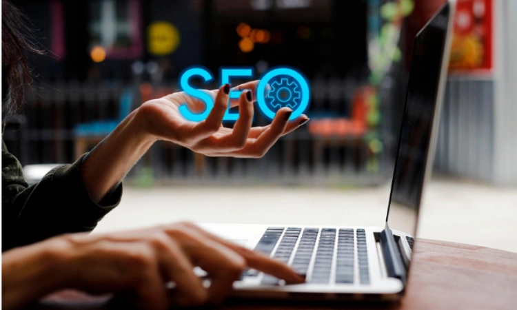 Mano sosteniendo la palabra SEO frente a una laptop en entorno urbano.