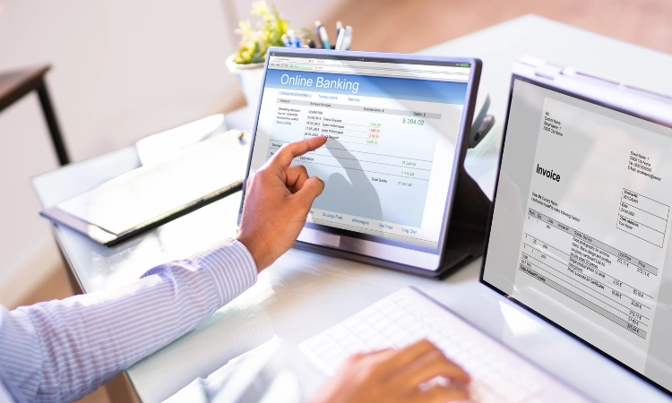 Persona gestionando pagos y facturas en línea desde una tablet y computadora, representando soluciones digitales de banca y facturación para negocios.
