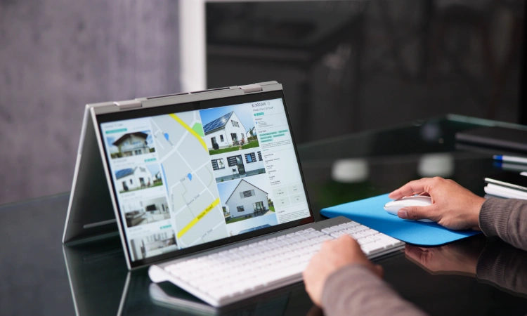 Persona usando una laptop convertible para navegar un sitio web inmobiliario con mapa y propiedades en venta.