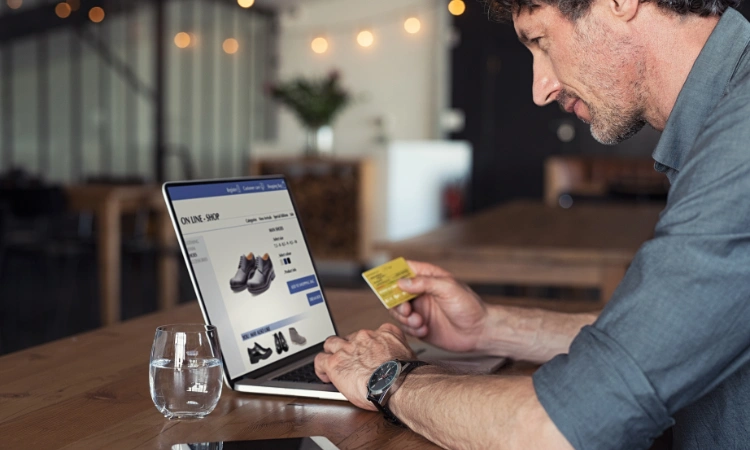 Hombre realizando compra online con tarjeta de crédito en su laptop en un ambiente moderno y acogedor.