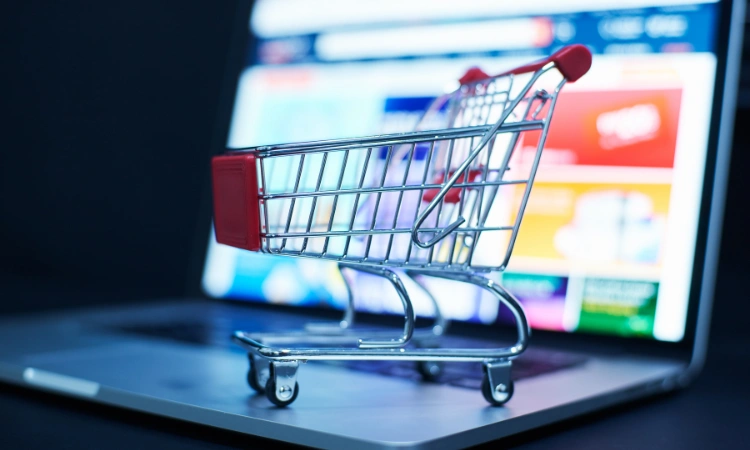 Carrito de compras en miniatura sobre una computadora portátil con pantalla de tienda en línea.