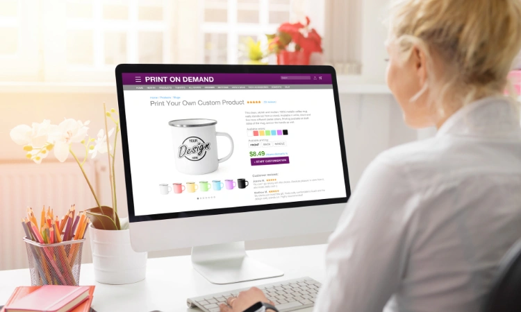 Mujer trabajando en diseño de taza personalizada en plataforma de impresión bajo demanda desde computadora de escritorio.