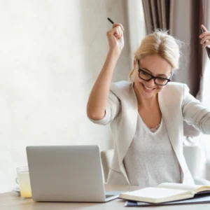 Mujer feliz celebrando frente a su laptop mientras trabaja desde casa.