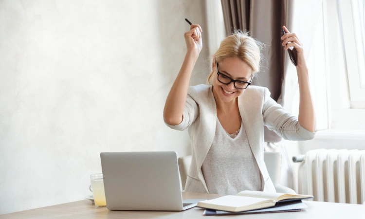 Mujer feliz celebrando frente a su laptop mientras trabaja desde casa.